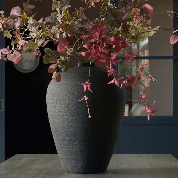 Oversized black vase on a table with flowers